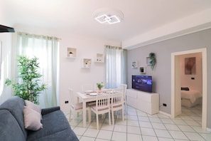 Ein modernes Wohnzimmer mit Sofa, Esstisch, Stühlen, Fernseher und einer Zimmerpflanze.