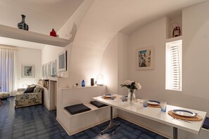 A modern living room with a sofa, a dining table with plates and glasses, and a fireplace. - SANREMO VISTA MARE - Elegante (Sanremo)