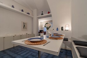 A modern dining area with a white table set for two, featuring woven placemats and blue plates.