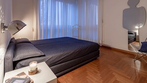 A neatly made bed with a dark cover, a bedside table with a candle, and a chair.