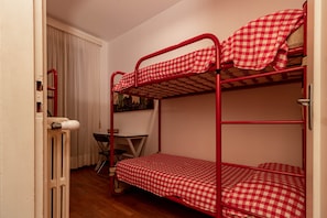 A bunk bed with a checkered bedspread, a small table with a chair, and a radiator. - SANREMO VISTA MARE - Elegante (Sanremo)