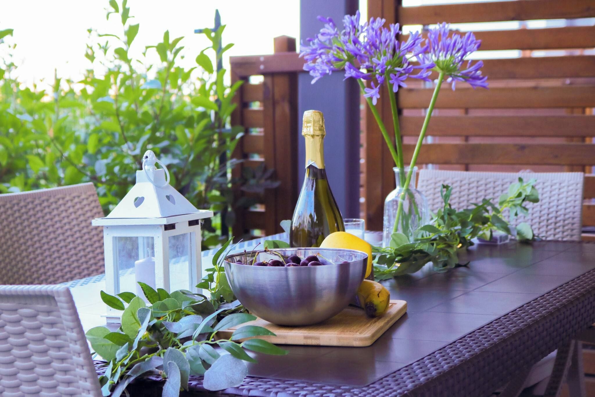 A table with a bottle, a bowl of cherries, a lemon, and a lantern.