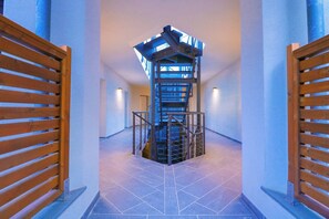 A modern interior with a central spiral staircase, flanked by wooden gates, and a tiled floor.