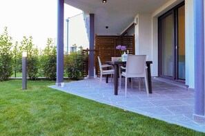An outdoor patio with a table and chairs, a grassy area, and a building with a sliding glass door.
