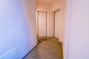 A narrow hallway with two doors, a radiator, and a tiled floor.