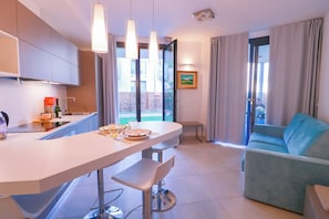 A modern kitchen with a dining area, a sofa, and a view of the outdoors.