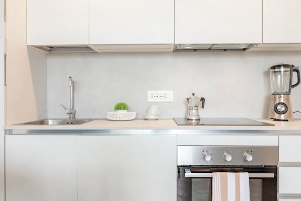 A modern kitchen with a stainless steel sink, a coffee maker, a blender, and an oven.