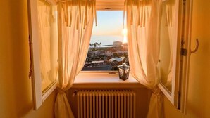 Une chambre avec vue sur la mer au coucher du soleil, vue Ă travers une fenĂȘtre ornĂ©e de rideaux.