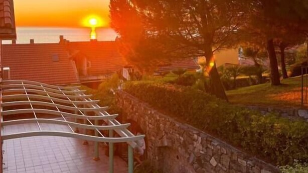 Une vue sur le coucher de soleil depuis un balcon dotĂ© dâun mur en pierre et dâune rambarde en mĂ©tal.