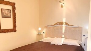 Un lit bien fait, recouvert dâune couverture marron, avec une tĂȘte de lit ornĂ©e dâun motif dĂ©coratif, une table de chevet avec une lampe et un tableau encadrĂ© accrochĂ© au mur.