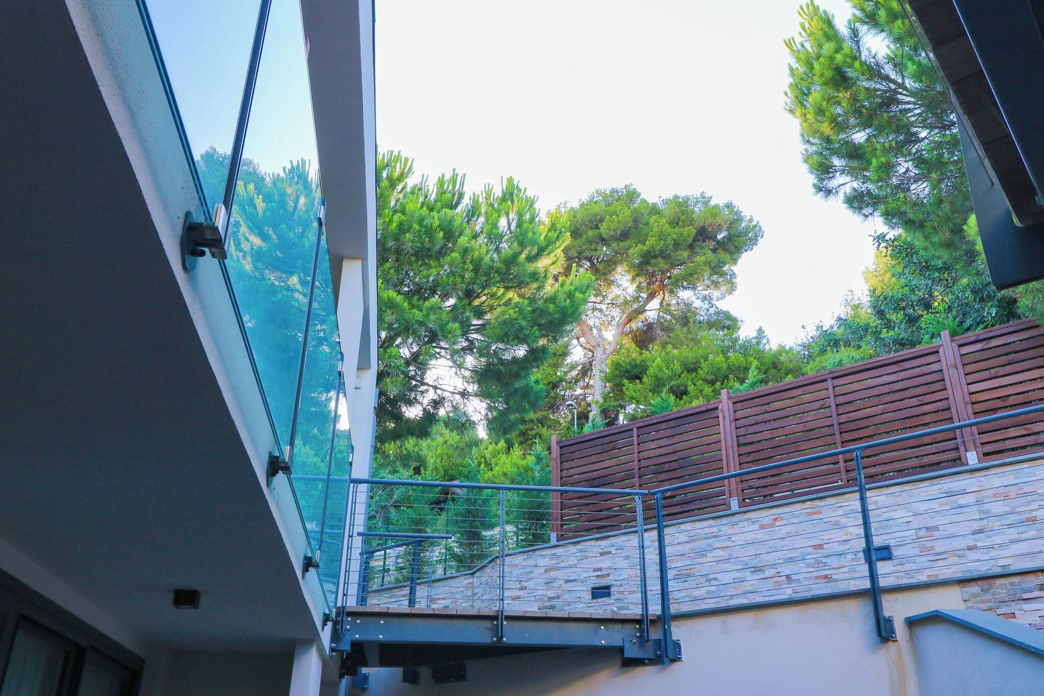A modern building with a glass facade, a stone wall, and a wooden fence overlooking a green landscape.