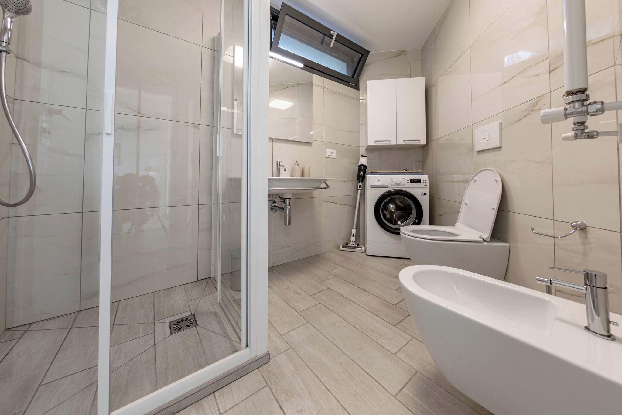 Een moderne badkamer met een douchecabine, een ingebouwde wasmachine, toilet en wastafel.