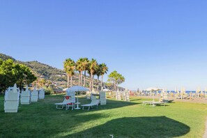 A grassy outdoor area with white lounge chairs and umbrellas, a small table, and a white tent.