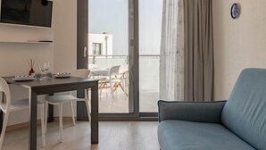 Une chambre dâhĂŽtel moderne avec un balcon, un coin repas avec des chaises et une table blanches, et un canapĂ© bleu.