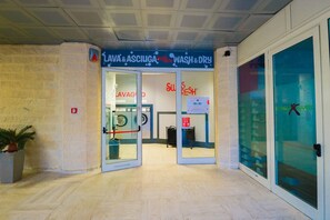 Une laverie en libre-service avec des portes en verre et une enseigne indiquant « LAVA & ASCIUGA » et « SWISS FRESH WASH & DRY ».