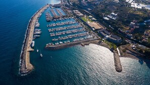 Vue aĂ©rienne dâune marina oĂč sont amarrĂ©s de nombreux bateaux, avec une digue en pierre et des bĂątiments rĂ©sidentiels et commerciaux environnants.