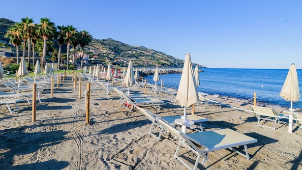Une plage bordée de rangées de chaises longues et de parasols, un ciel bleu dégagé et un paysage vallonné en arriÚre-plan.