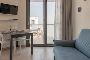 A modern living room with a sofa, a dining table with chairs, and a balcony with a view.