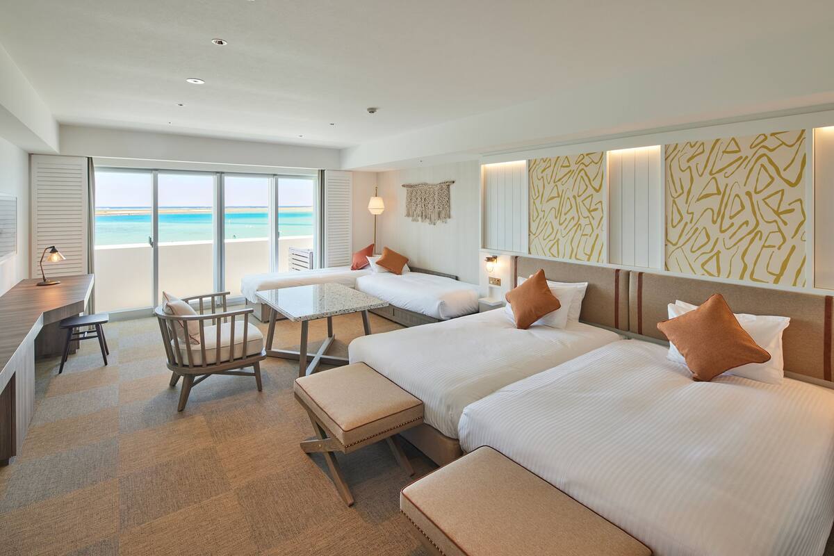 Habitación de hotel con dos camas, un escritorio, una silla y vista a la playa.