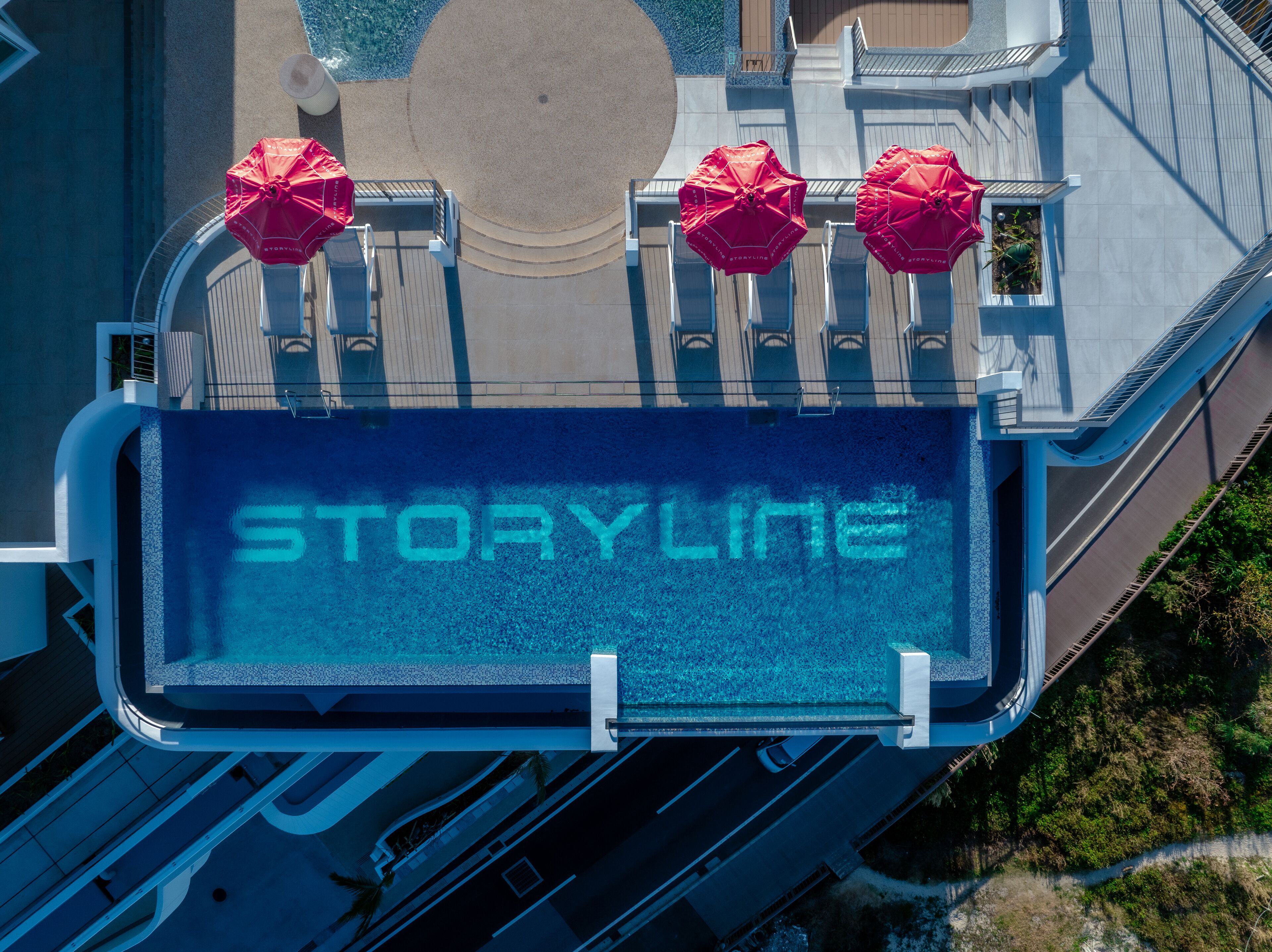 Ein Poolbereich auf dem Dach mit dem Schriftzug „STORYLINE“ auf dem Boden, umgeben von Geländern und roten Sonnenschirmen.