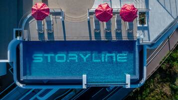Ein Poolbereich auf dem Dach mit dem Schriftzug „STORYLINE“ auf dem Boden, umgeben von Geländern und roten Sonnenschirmen.