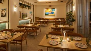 A spacious restaurant with multiple dining tables and chairs, a ceiling fan, and a large painting on the wall.