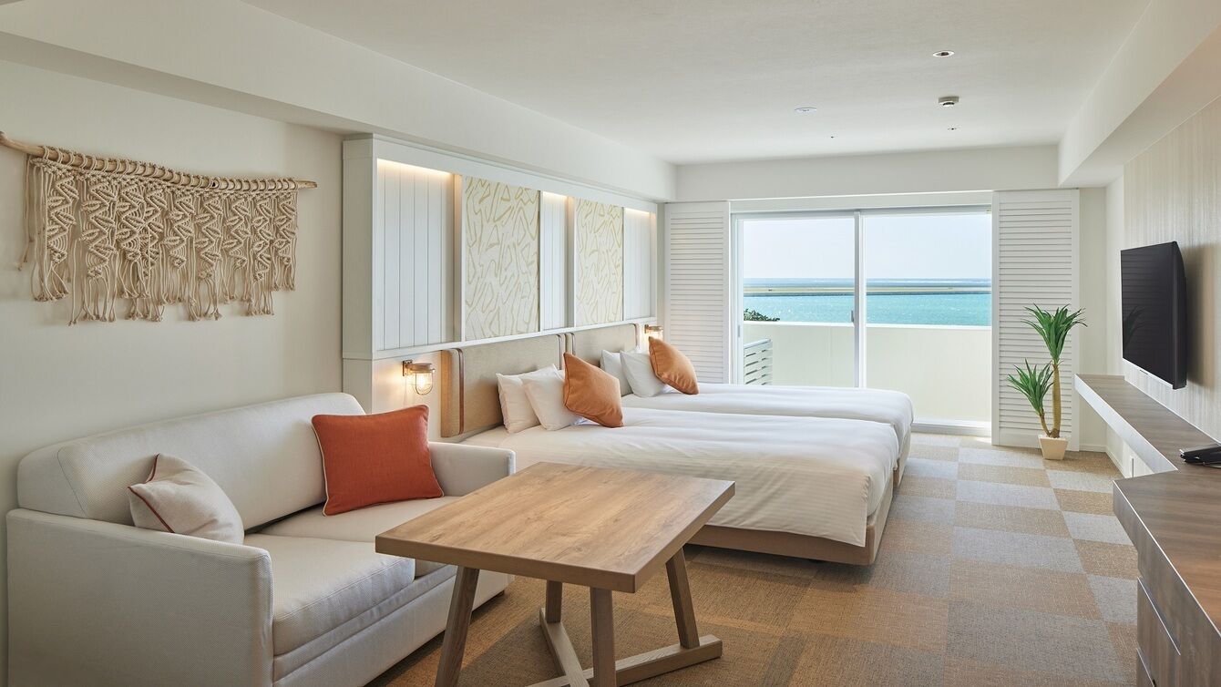 Een moderne hotelkamer met een groot bed, een sofa, een kleine tafel, een televisie en een balkon met uitzicht op zee.
