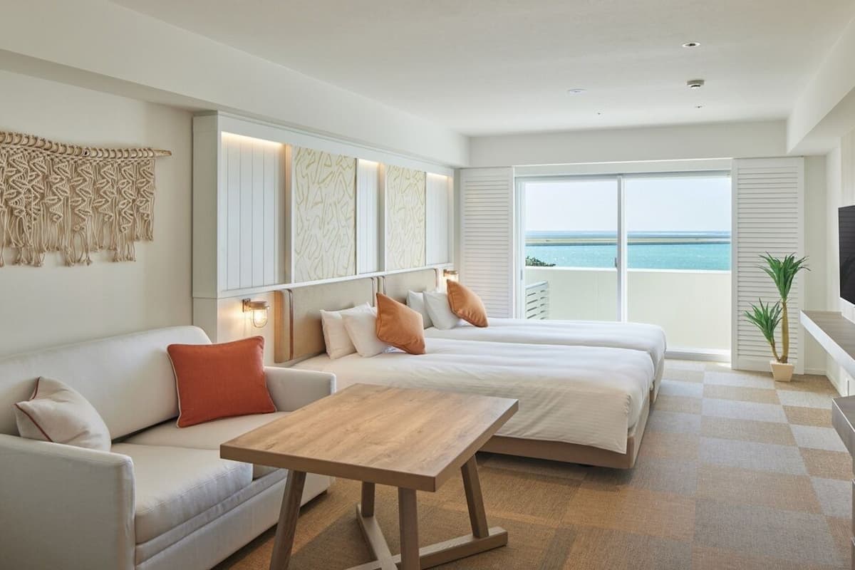 Habitación de hotel moderna con una cama grande, un sofá, una mesita, un televisor y un balcón con vistas al mar.