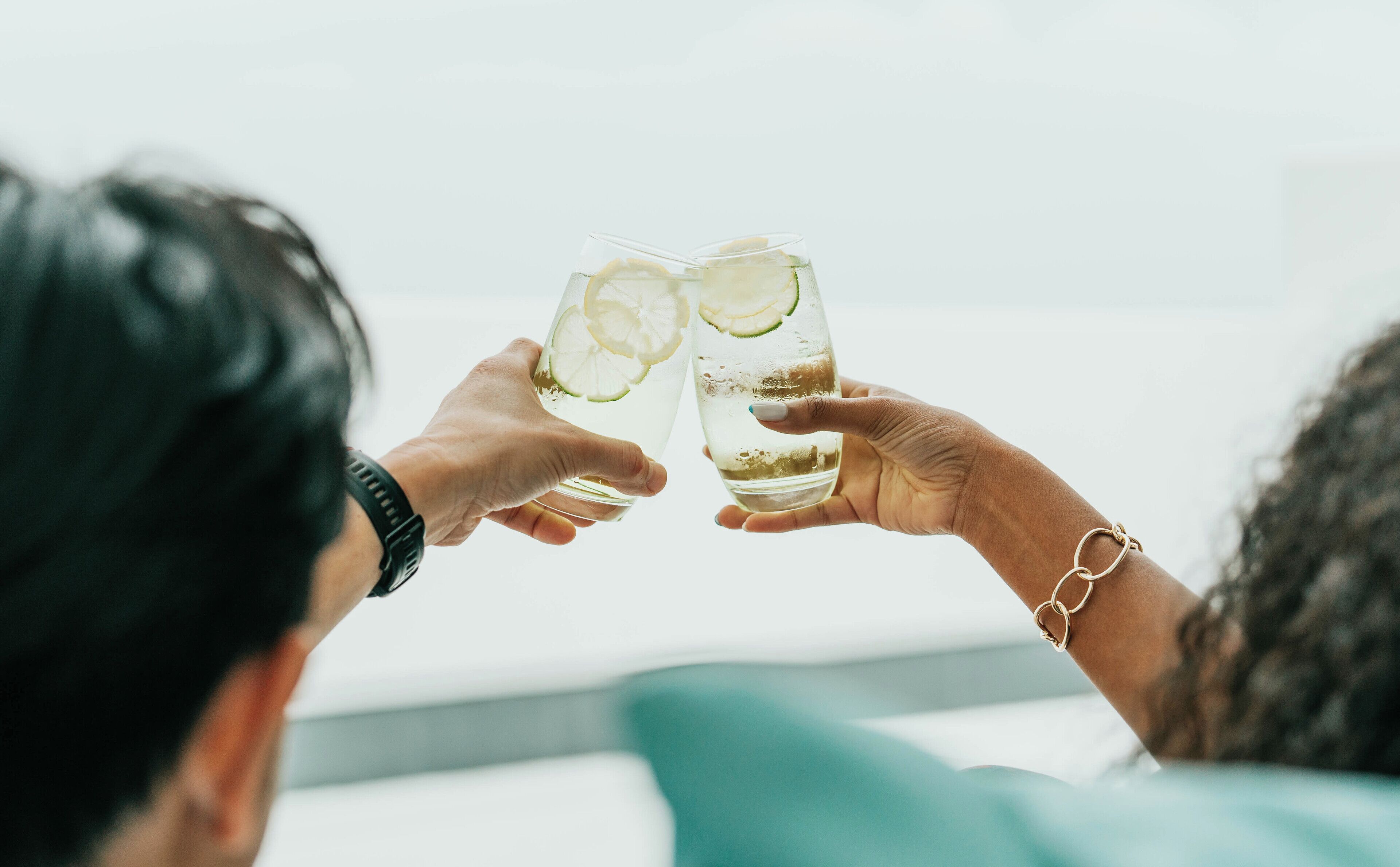 Two people holding glasses with lime slices.