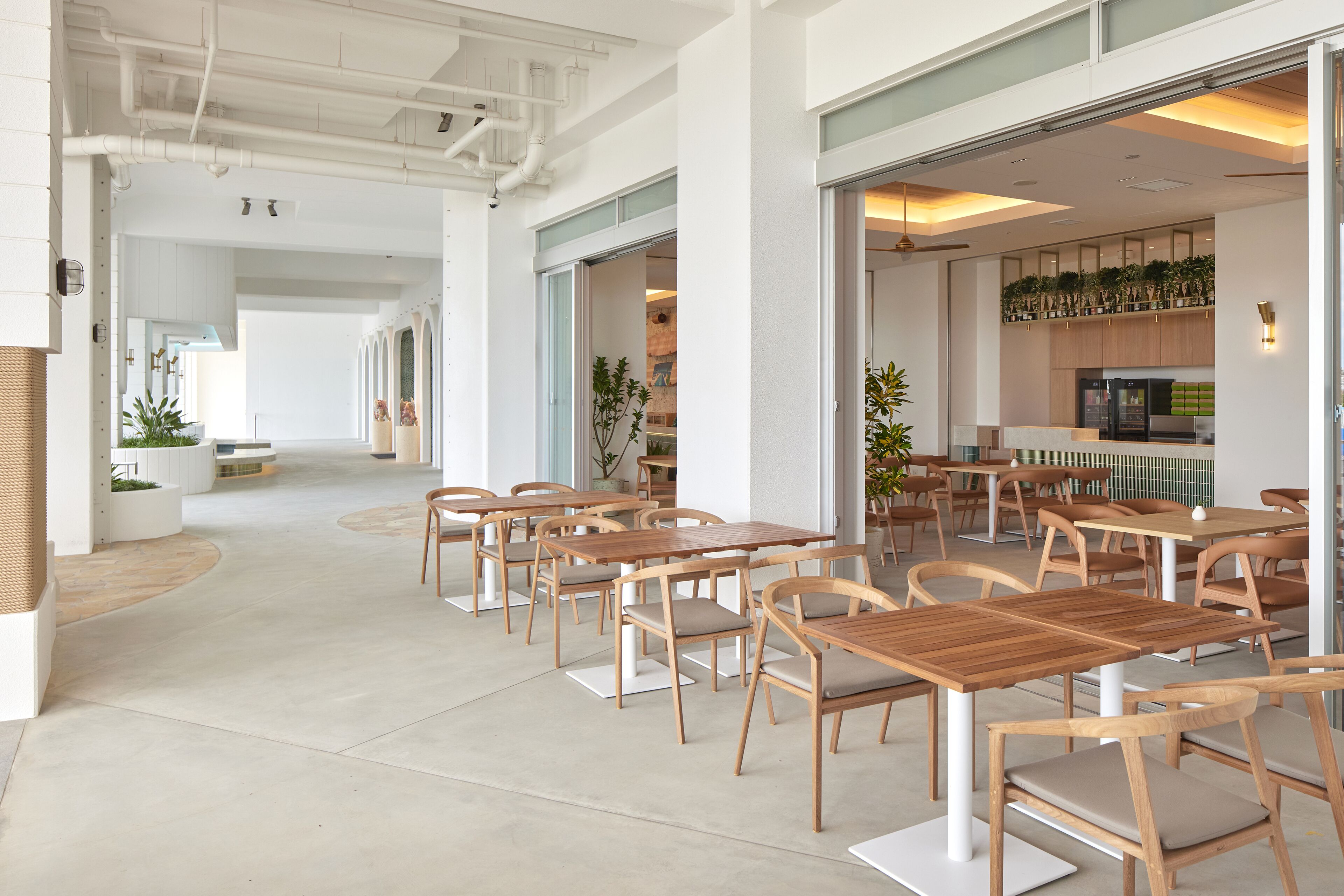 A modern dining area with wooden tables and chairs, a kitchen in the background, and a clean, open floor plan.