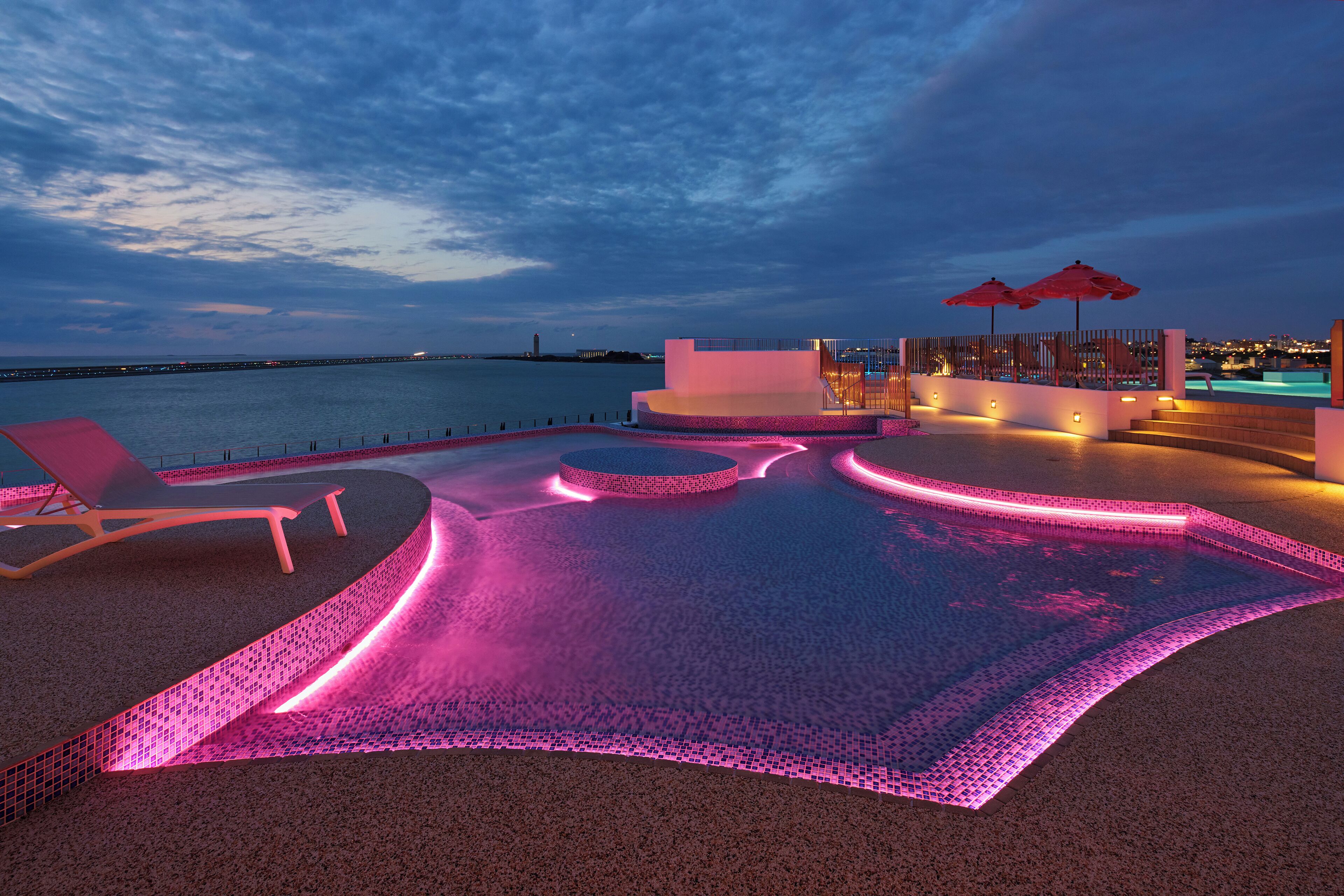 A pool area with a curved design, lounge chairs, and umbrellas.