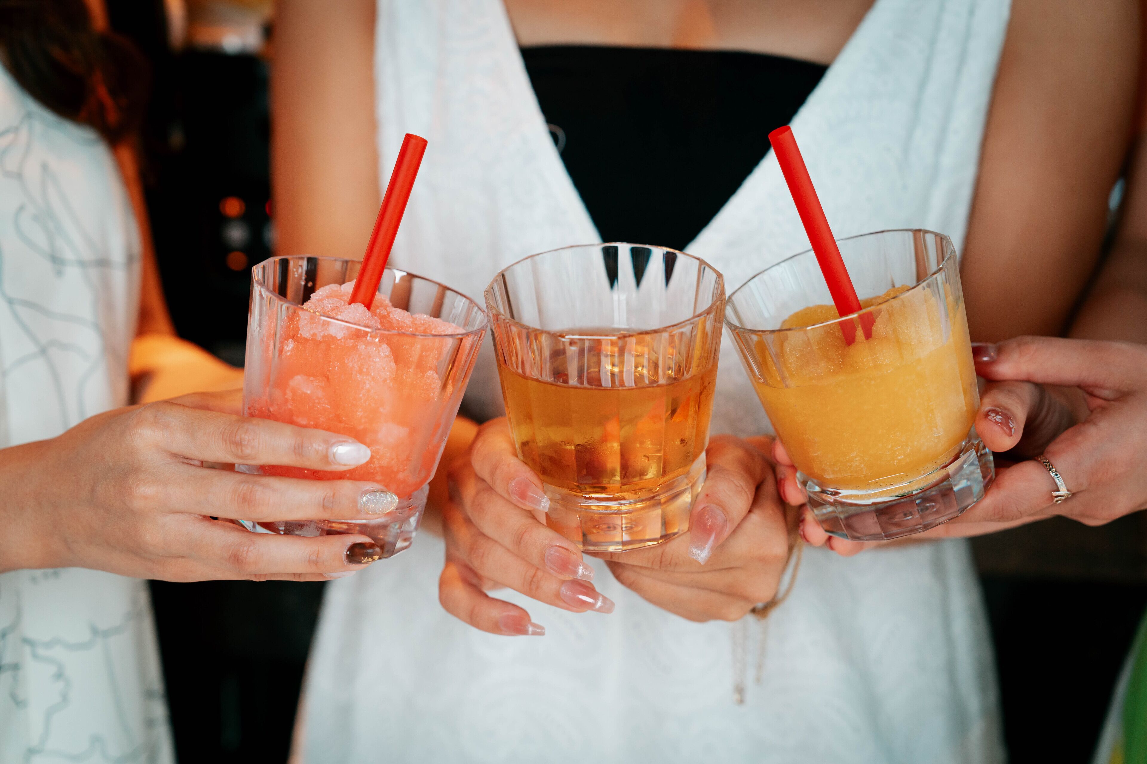 Three people holding glasses of different colored beverages with red straws.