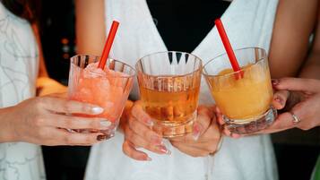 Three people holding glasses of different colored beverages with red straws.