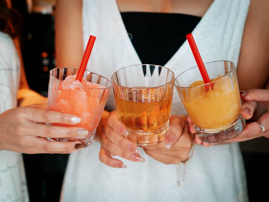 Three people holding glasses of different colored beverages with red straws.