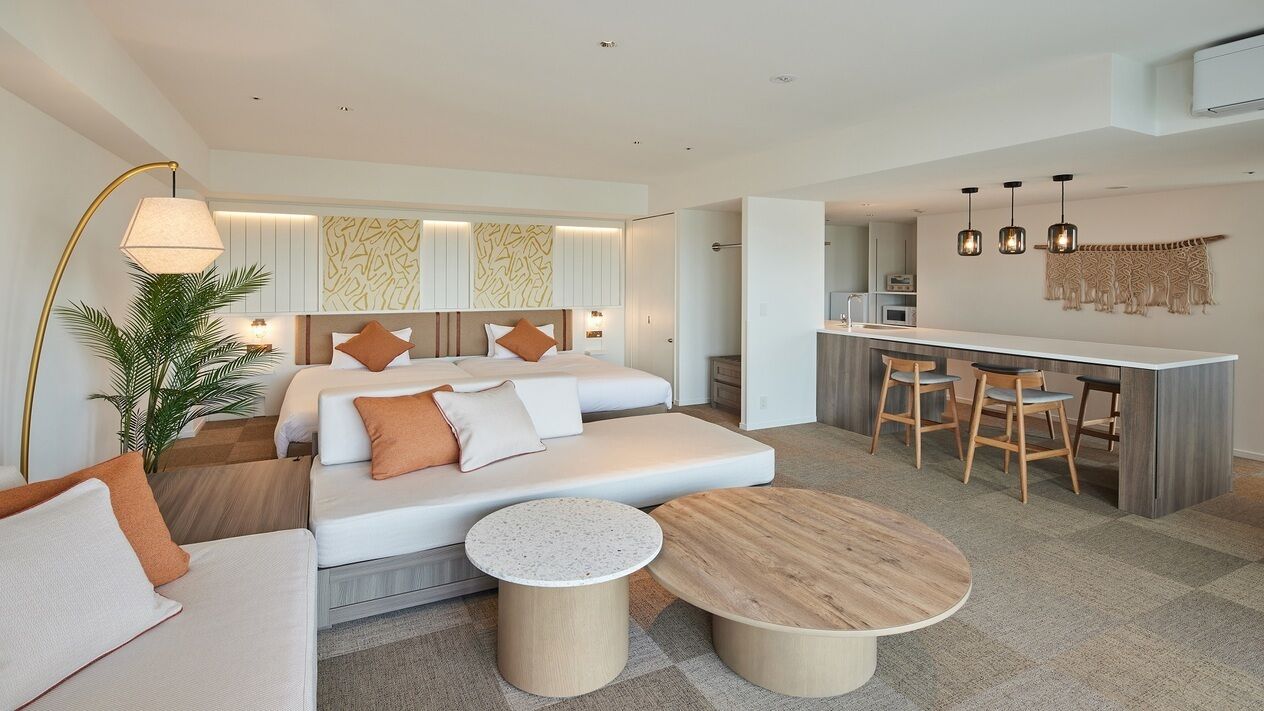 Een moderne hotelkamer met een slaapbank, een zithoek met barstoelen, een ronde houten tafel en een groot raam.