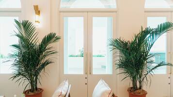 A room with two large potted palm trees, a white door with glass panels, and a wall-mounted light fixture.