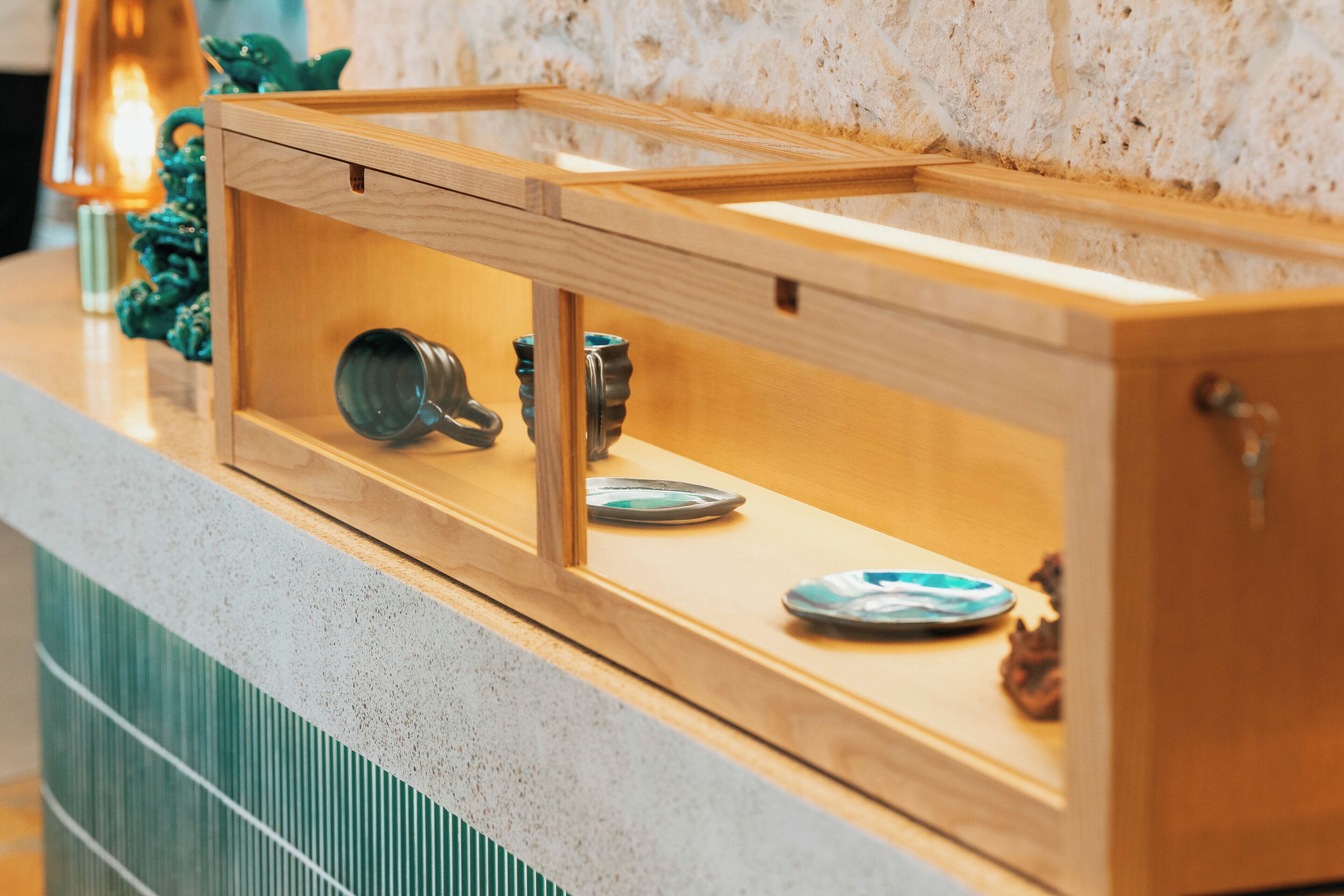 A wooden cabinet with a glass front, containing kitchenware and decorative items.