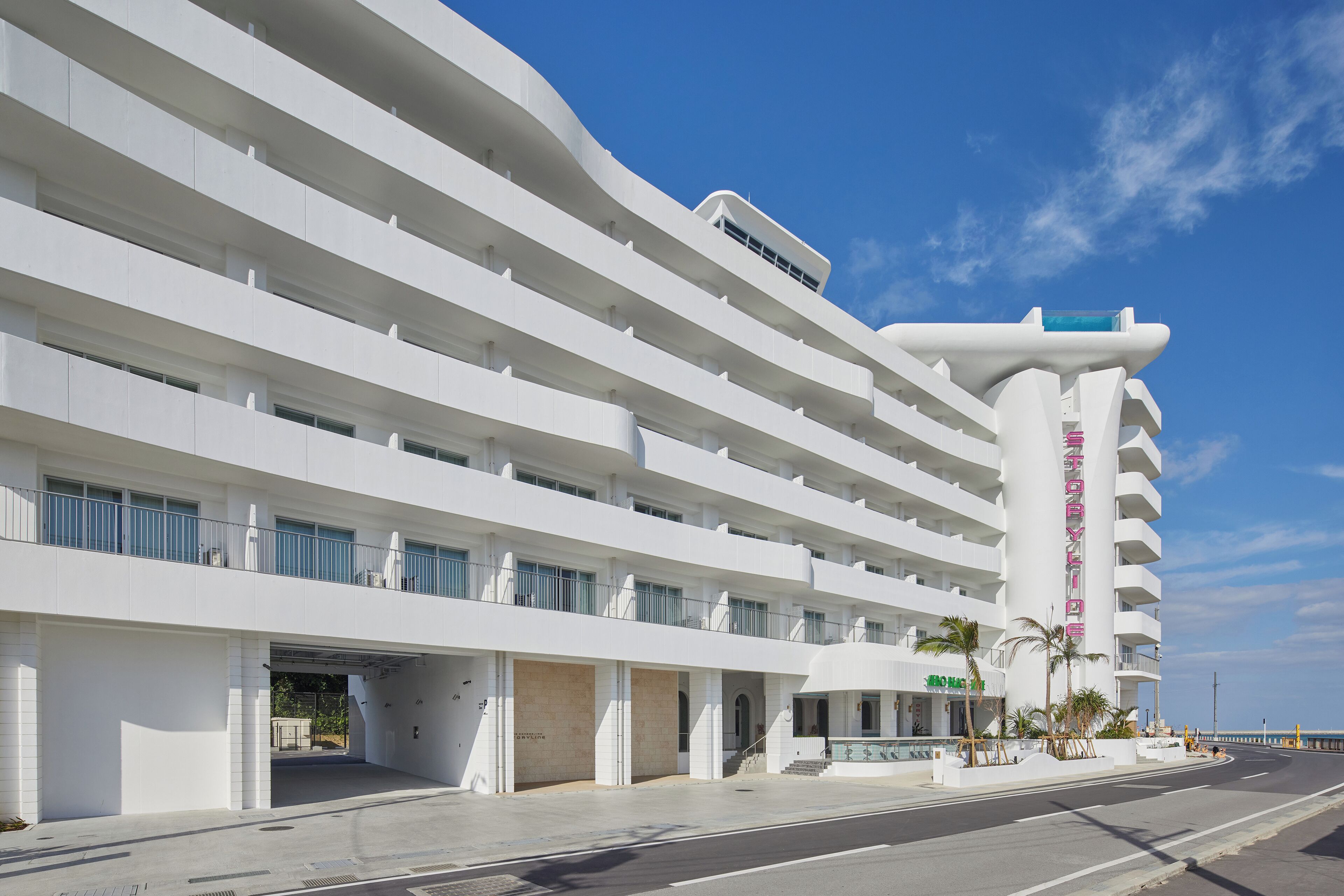 Un hotel moderno con varios pisos, un estacionamiento techado y vista al océano.