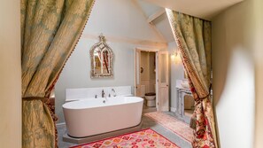 Une salle de bain avec une baignoire sur pieds, un miroir et une porte donnant sur une autre pièce.