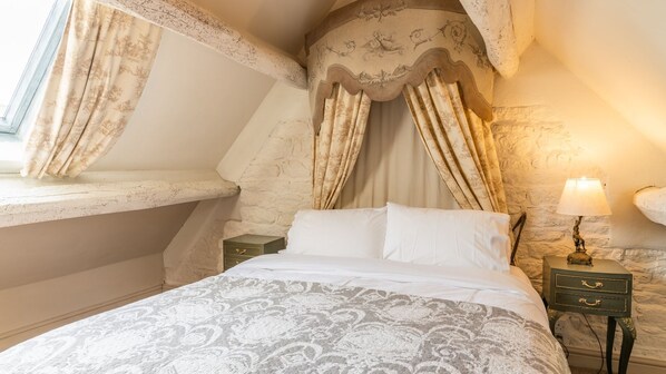 A bedroom with a bed, curtains, a nightstand, and a lamp. - Sixpenny Cottage - Spectacular views near Bourton-on-the-Water (Clapton-on-the-Hill)