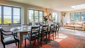 Un coin repas avec une table ronde dressée pour six personnes, entourée de chaises, et offrant une vue sur la verdure à l’extérieur.