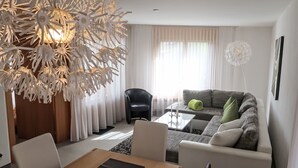 Ein modernes Wohnzimmer mit einer großen Kronleuchter, einer Sofagarnitur, einem Esstisch und einem schwarzen Sessel.