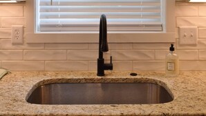 A kitchen with a granite countertop, a black faucet, and a window with blinds.