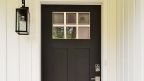 A dark brown front door with a small window above it, a keypad lock, and a welcome mat with "Welcome" written on it.