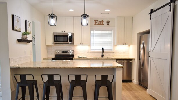 A kitchen with a central island, bar stools, a microwave, oven, refrigerator, and a sliding barn-style door.