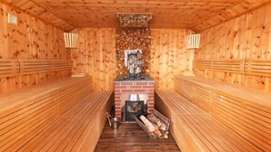 Sauna, jossa on puiset lauteet, tiilestä muurattu takka ja pino polttopuita.