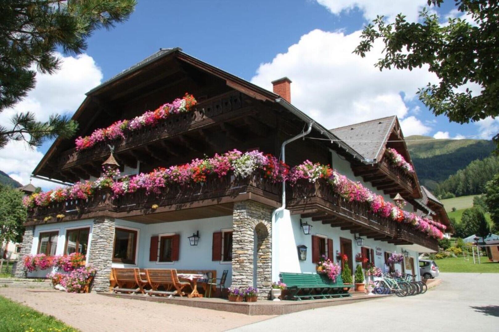 A traditional chalet with balconies adorned with flowers, stone walls, wooden shutters, and outdoor seating.