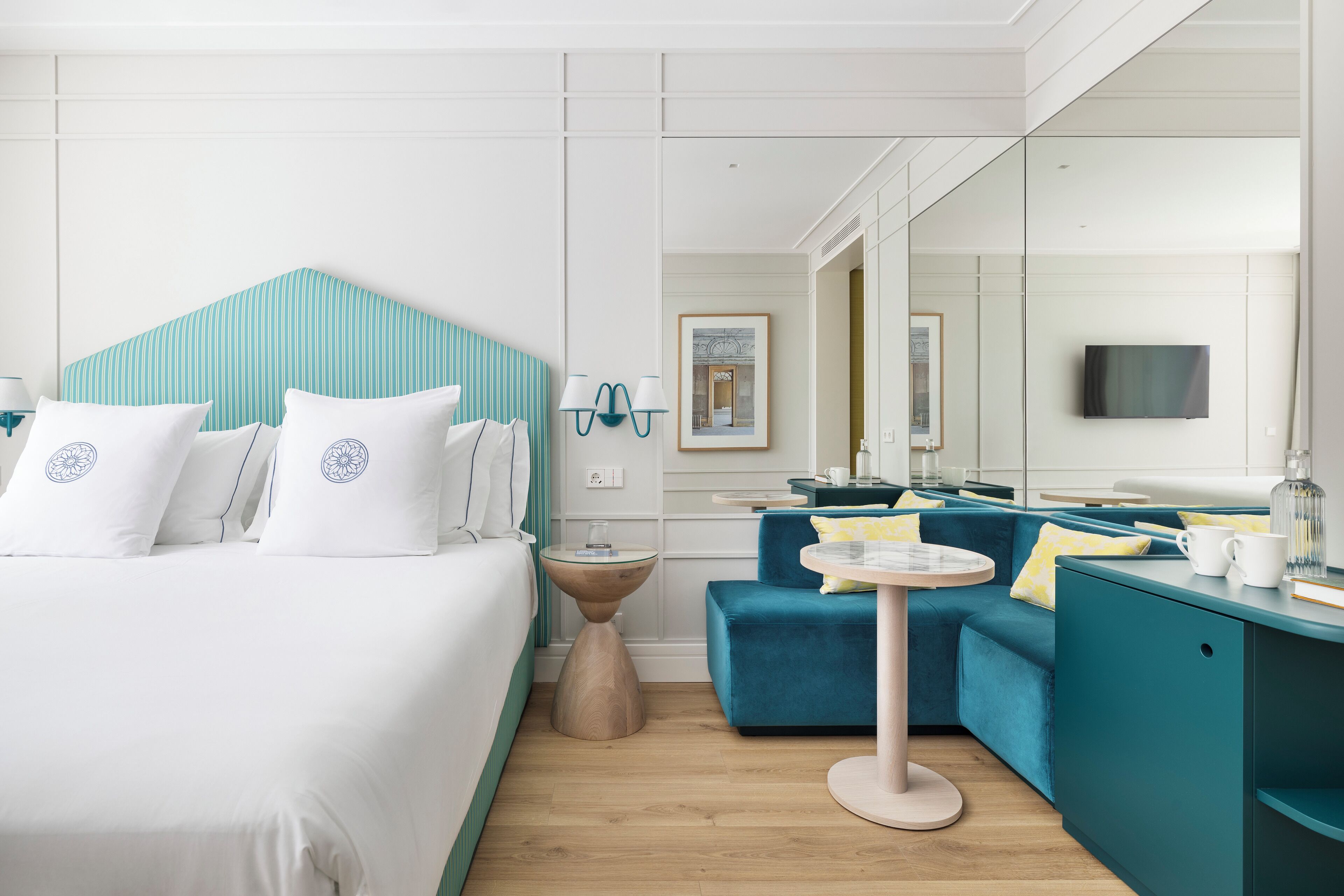 Ein Hotelzimmer mit einem Bett, einer Couch, einem kleinen runden Tisch, einem Spiegel und einem Fernseher.