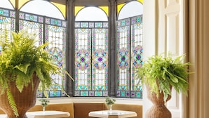 A room with a bay window, a sofa, and two large potted plants. - One Shot Palácio Cedofeita  (Porto)