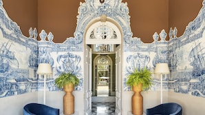 A lobby with a tiled wall, a chandelier, and two potted plants. - One Shot Palácio Cedofeita  (Porto)